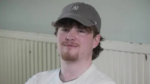 Claudia Sermbezis/BBC Friend Toby Keary pictured at the University of Southampton where he is a student. Toby is wearing a grey cap and has dark tousled hair. He is looking to camera and is wearing a white t-shirt.