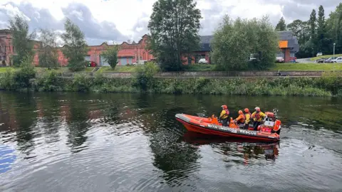 University of Strathclyde A rescue lifeboat moves along the still waters of a river past some industrial buildings in the background