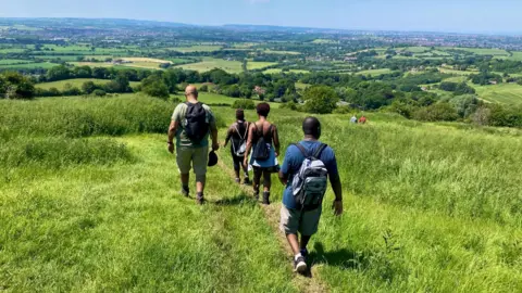 @celie Nigoumi A group of people walking on a hill in the countryside.