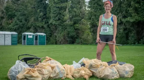 Stroud District Council Gill Thomas is standing on a lawn with rubbish bags in front of her. She is wearing a running outfit and is smiling at the camera.