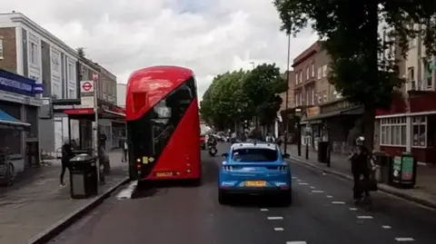 A blue car overtakes a bus while a cyclist comes the other direction 