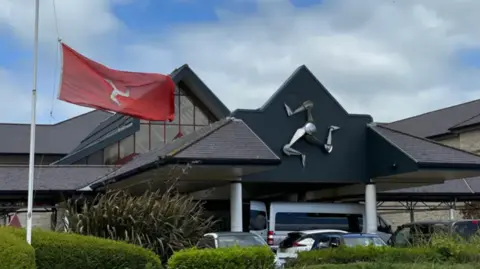 BBC Outside shot of Noble's Hospital in Braddan. An Isle of Man flag waves in front of the front door along with parked cars.