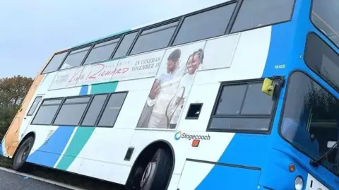 A bue and white double-decker bus on its side in a ditch after leaving the road