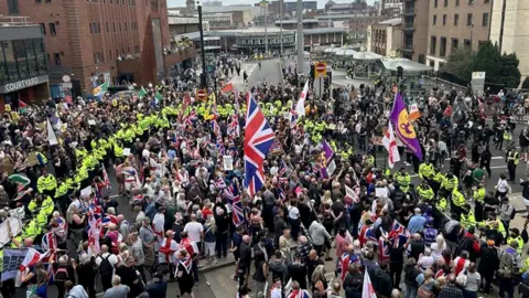 Crowds with flags attend the protest surrounded by police in high-vis jackets