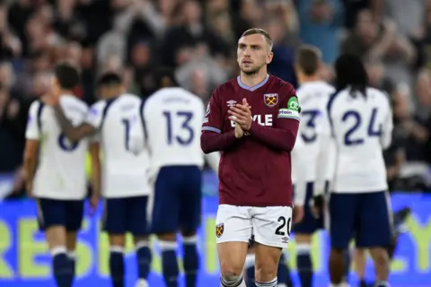 Reuters Jarrod Brown on a football pitch wearing a West Ham kit and clapping with Tottenham players in the background