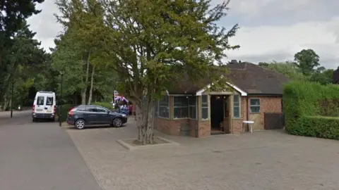 Google A Google Streetview image of the brick-built cafe surrounded by trees. There is a car parked and a Union Flag in the background.