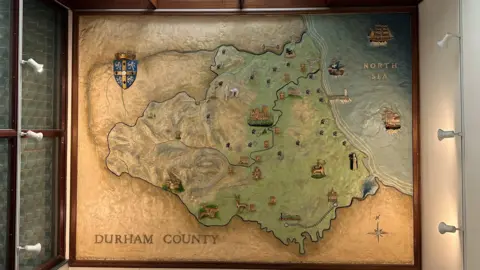 A 3D mural attached to a wall shows a map of Durham County in muted colours.