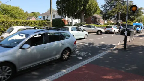 Deep South Media Cars pass a zebra crossing on a residential street lined with hedges and houses