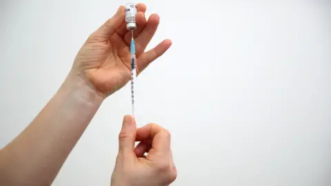 A person holding a syringe and the vaccine in another hand.