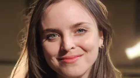 Fiddle player Laura Jane Wilkie, a young woman with long brown hair and blue eyes smiles during her interview in a music studio.