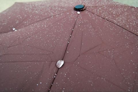 Rain drops sit atop an open, brown umbrella