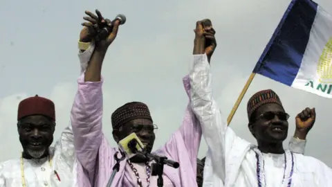 AFP via Getty Images Buhari, his running mate Chuba Okadigbo and Chairman of the All Nigerian Peoples Party Don Etiebet, smile and raise their joined hands above heads.