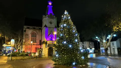 Banbury Town Council Banbury Town Hall with purple lights on the building and a Christmas tree covered in bright lights in front of the building.