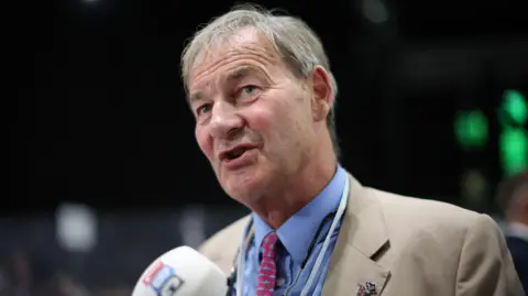 EPA Rupert Lowe wearing a blue shirt, red tie and beige jacket.