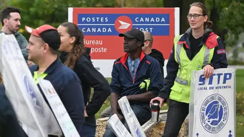 A Bloomberg recebe a equipe postal que atinge as imagens, algumas marcas de piquetes brancos e azuis se reuniram em frente a uma grande marca dos correios azuis e vermelhos do Canadá para ler 'STTP, de Montreal local'.