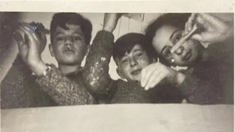 Duschenes family A black and white picture dating back to 1930s of three boys controlling puppets which are out of shot. The boys are all wearing the same top and are looking down intently.