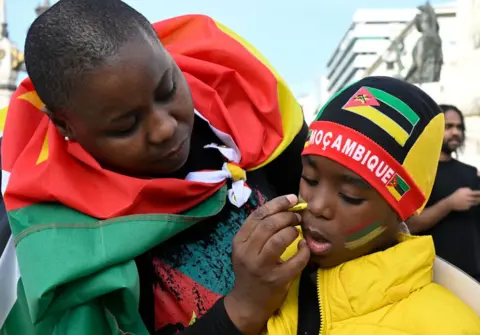 Horacio Villalobos / Getty Images A picture of a woman drawing the Mozambican flag on a boy's face - Saturday 16 November 2024