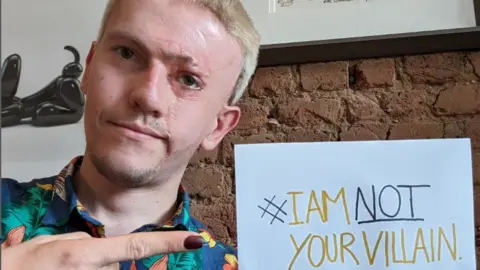 Changing Faces UK Actor Robert Rhodes holds a sign reading 'I am not your villain'