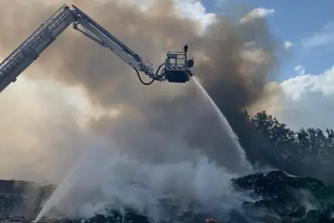 Derbyshire Fire and Rescue Service An aerial ladder platform hosing down a pile of smouldering waste
