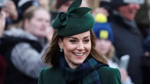 Reuters She is smiling and wearing dark green and a matching green hat. She has a green and navy checkered scarf around her neck.