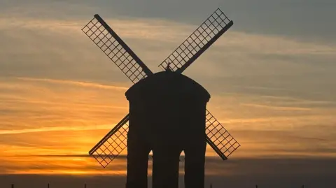 Nana Dee / BBC Weather Watchers A windmill in silhouette in Fenny Compton with sun setting behind it