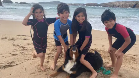 Family photo Mali the dog lying on a sandy beach with Sarah Recinos Ralda's four children 