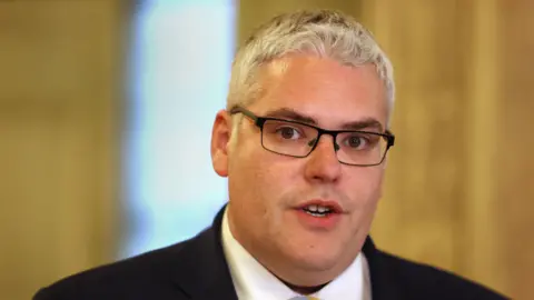 PA Media Gavin Robinson in black suit and white shirt. He has grey hair and wears glasses.