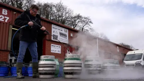 BBC Philip Thomas jet-washes a row of silver and green beer barrels outside his brewery on the Treforest industrial estate.
