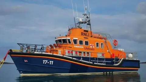 A view of the St Mary's lifeboat. It is blue at the bottom and orange at the top. It has the numbers 17-11 at the front and 'RNLI' at the top.
