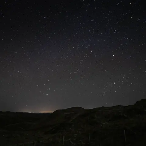 Siân Harrison The night sky full of stars including Orion's Belt in the bottom tright hand corner of the frame just above the horizon.