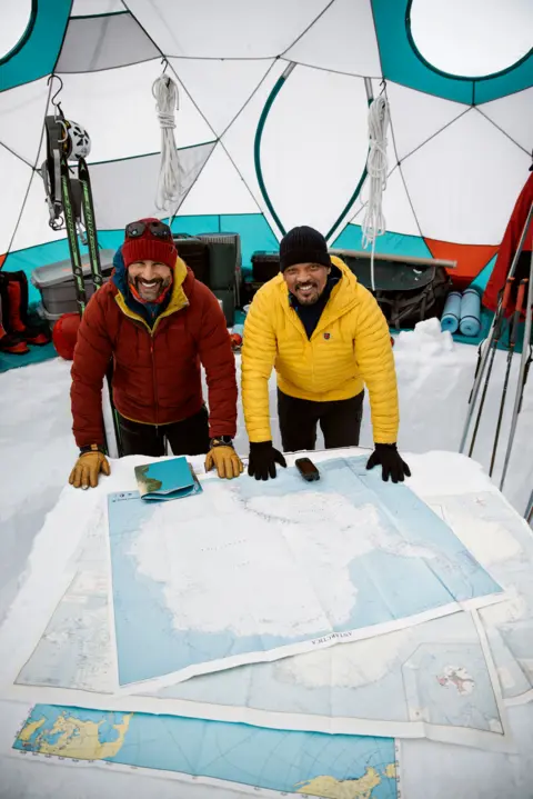 National Geographic/Freddie Claire Will Smith and Richard Parks are leaning on a large table, with large maps of Antarctica on top. They are stood in a large tent with camping gear surrounding them.