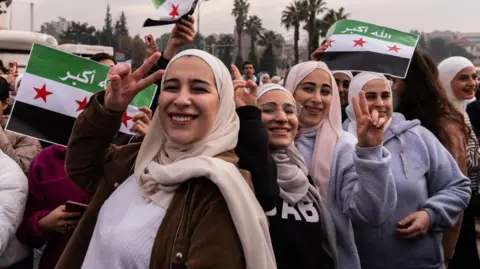 Emin Sansar/Getty Images Syrians waving flags in Umayyad Square, Damascus, to celebrate the collapse of the Assad regime. Several women are making a victory sign at the camera.