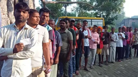 Election Commission of India Men line up with their voter identity cards in hand outside a polling station in Bihar's Taraiya
