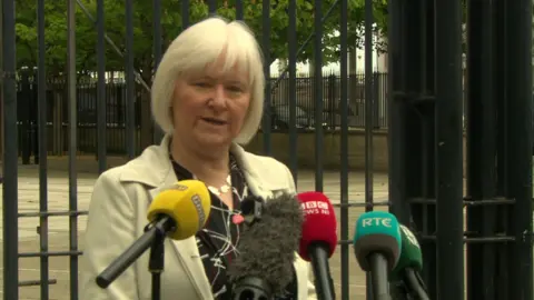Det Insp Michelle Griffin. She has a white bob with fringe, wearing a cream coat and black blouse. She is standing in front of microphones.