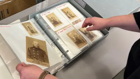 LFB A binder full of old photographs of firefighters. Their names are written in red above the images. 