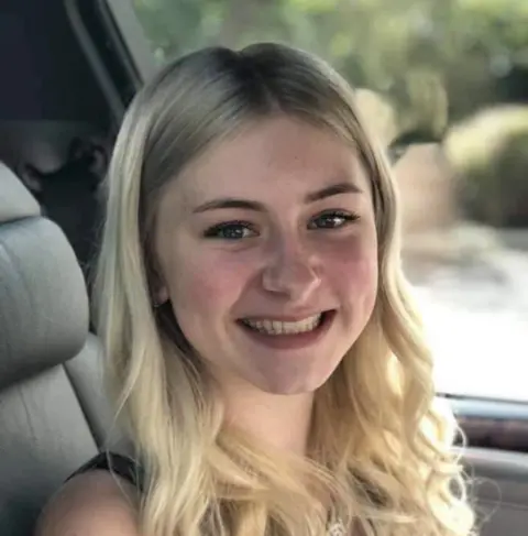 Laionie Kennard, with long blonde hair, smiling at the camera, sitting in a car