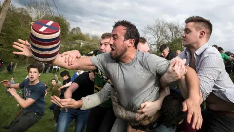 Getty Images Men in a field grappling to grab a beer barrel. 