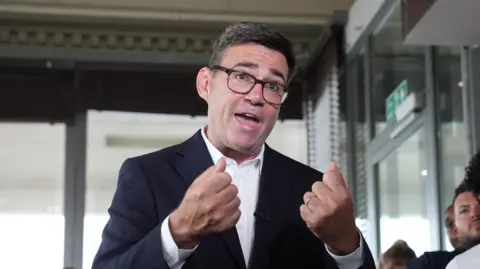 PA Media Newly confirmed Labour Party leader Andy Burnham speaking in a black and white suit with his fists held out passionately in front of him.  