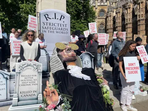 PA Media Protesters opposing the bill gather outside Parliament with placards, a puppet judge and a mock gravestone reading: "RIP strictest safeguards in the world".