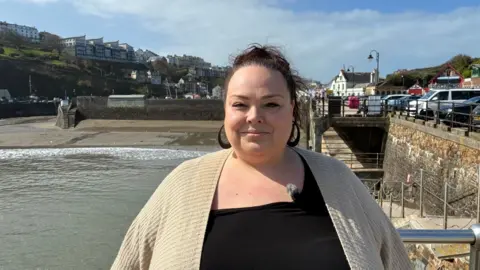 Charmain Lovett in a black top and a beige cardigan with Ilfracombe harbour in the background