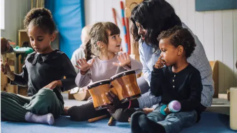 A teacher plays a pair of bongo drums with three small children