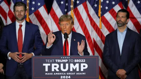 Republican presidential candidate and US President Donald Trump speaks accompanied by his sons Eric Trump and Donald Trump Jr during his caucus night watch party in Des Moines, Iowa, 15 January 2024