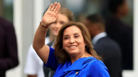 Peruvian President Dina Boluarte, wearing a bright blue dress, waves to the press as she arrives at the United Nations Ocean Conference in Nice, France