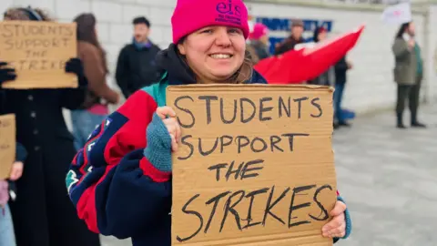 A picket line at University of Aberdeen with a student holding up a cardboard sign that reads: "Students support the strikes".