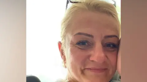 Beata Szauer, with an arm up to her face, with tied back blonde hair. She has a pair of glasses on her head. She is smiling at the camera. 