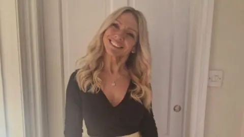 Family handout Claire Butler seen with long wavy blonde hair and smiling at the camera. She is wearing a black top with a gold skirt in front of a white doorway.