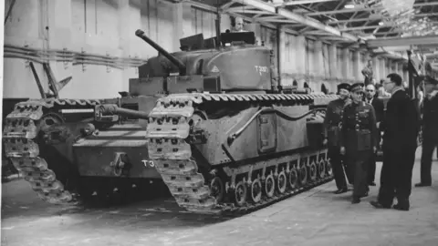 Vauxhall Heritage Men in uniform and suits inspecting a tank which is at the end of an assembly line in a factory