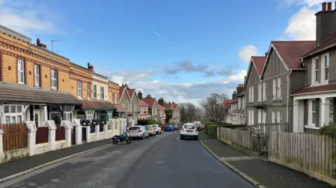 Emma Draper Street-view picture of Marathon Road. It's a blue sky with cars and motorbikes parked on the edge of the road. 