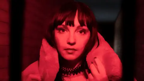Mary Mina Red and black press image of Mary Mina who is wearing a fur coat and has dark hair