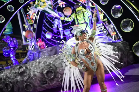 Tita Barros / Reuters A woman performs in a silver costume in front of a space themed display